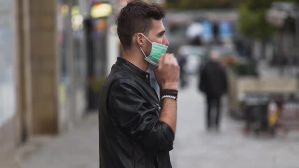 A young man in a leatherette jacket with a modern hairstyle on a busy street, putting on a green pro
