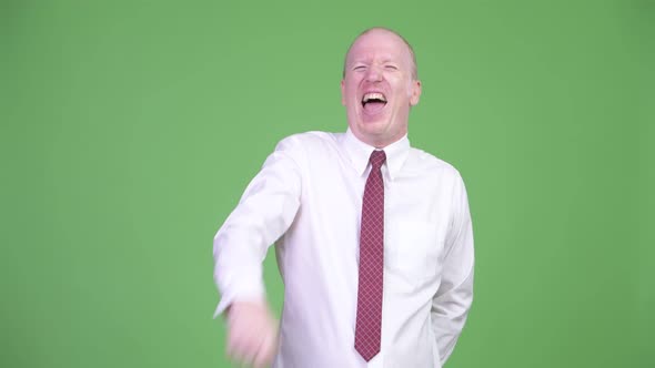 Happy Mature Bald Businessman Laughing While Pointing Finger