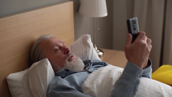 Tracking Shot of Handsome Bearded Mature Adult Male Lying on Bed in Hospital and Talking on Mobile