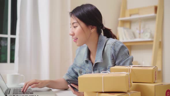 Asian young woman owner of SME online checking product on stock and save to laptop working at home.
