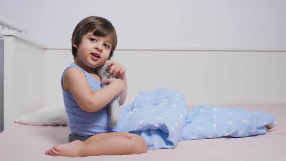 Child Is Sitting on the Bed in a T-shirt and Playing