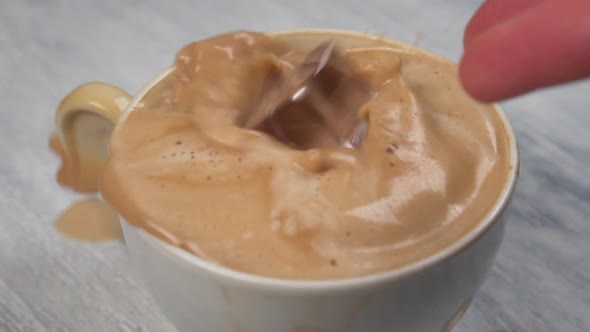Handful of ice cubes falls into a glass with coffee with splashes and spills 