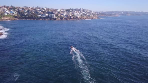 Aerial fly over drone following a speed fishing boat at the Sydney coastal beach seaside