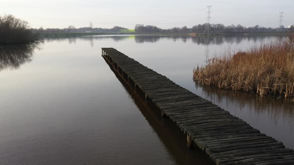 Aerial,showing a large wooden jetty at a moody day alongside golden reeds moving to a birds eye view