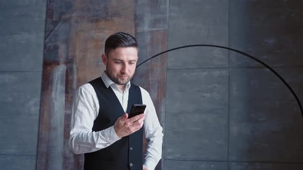 Successful Happy Businessman in a Luxurious Black Suit Sends Text Messages on His Modern Smartphone