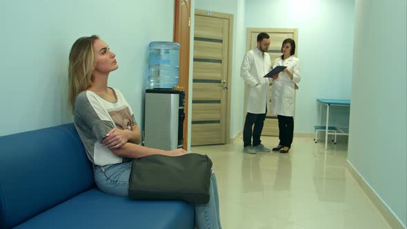 Female Patient Waiting in Hospital Hall While Two Doctors Consulting