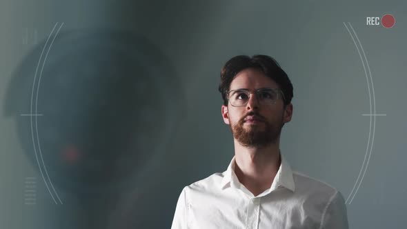 Young man worriedly looking around an interrogation room and being monitored by camera. Digital HUD