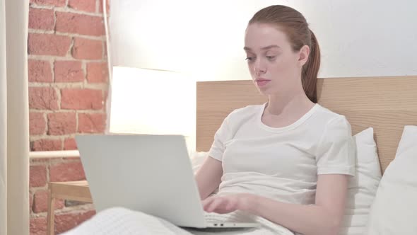 Redhead Young Woman Working on Laptop and Yawning in Bed 