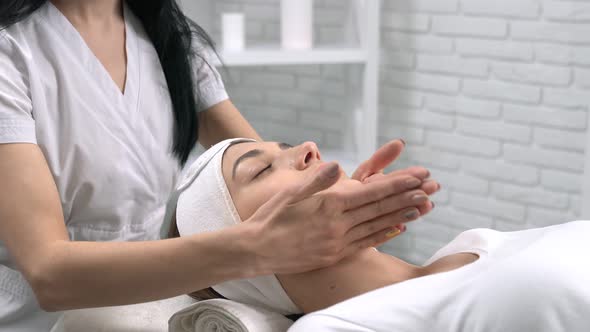 Woman Lying and Enjoying Procedure Face Massage in Salon