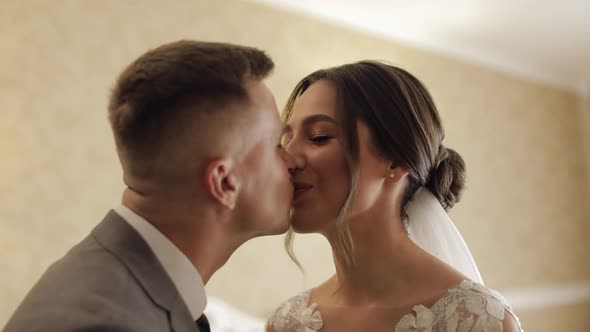 Newlyweds Young Caucasian Bride and Groom First Meeting at Wedding Day Making a Kiss Indoors