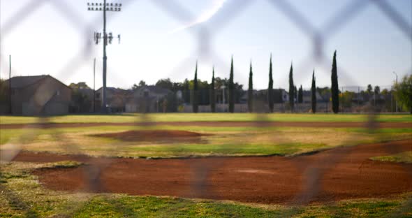 Slow slide left looking out on an empty green baseball field diamond from behind a chain link fence