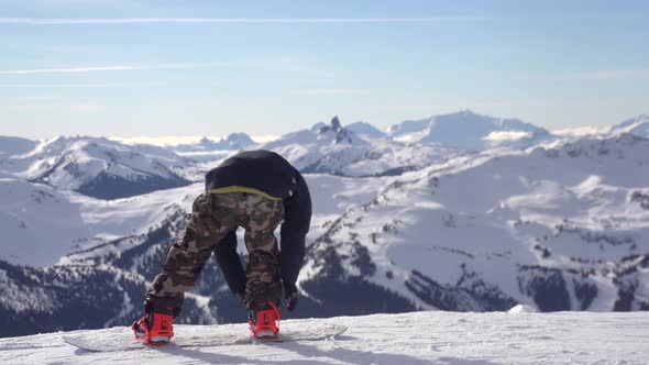 A young man snowboarder standing with his snowboard on a snow covered mountain.