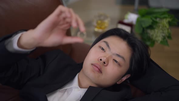 Headshot Portrait of Thoughtful Asian Young Man in Suit Looking at Wedding Ring in Hand