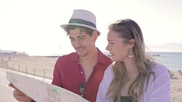 Young Hipster Couple Tourists Reading Map at the Beach on Vacation Sightseeing