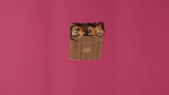 A Delicious and Unhealthy Chocolate Bar Rotates on a Pink Background. Bitten Sweets Isolated. The