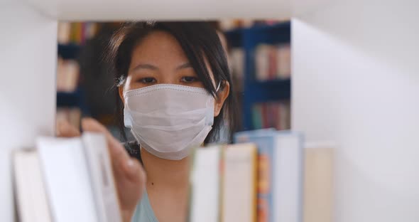 Asian University Student Wearing Protective Mask Choosing Book at Library