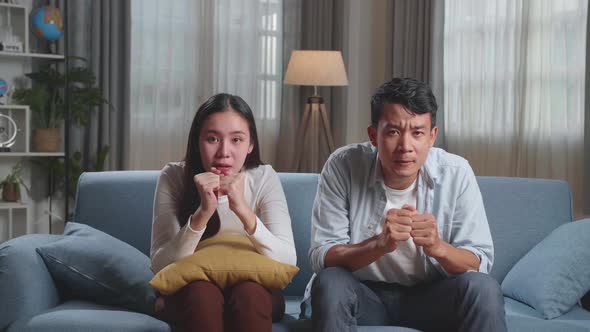 Excited Asian Couple Watching Tv Together Sitting On A Sofa In The Living Room At Home