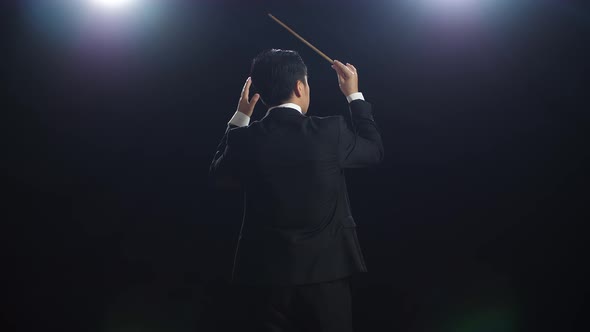 Back View Of Asian Conductor Man Holding A Baton And Showing Gesture In The Black Studio