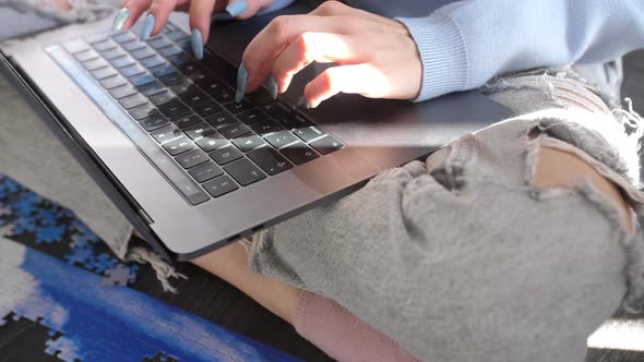 woman with long nails manicure typing modern laptop keyword device sitting cross legged wearing fash