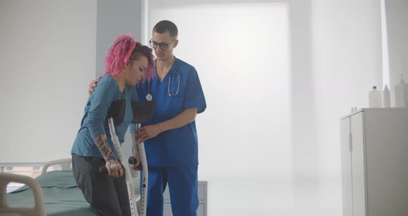 Doctor Helping Female Patient in Crutches at Hospital Ward