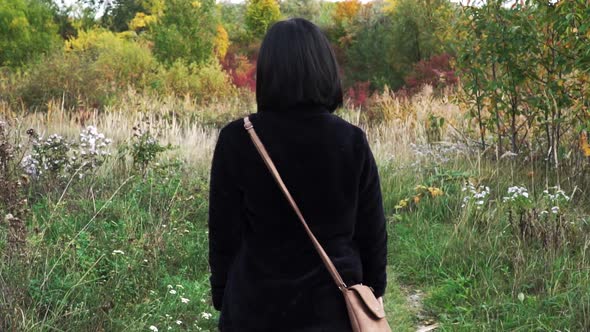 Following shot of girl walking through park with autumn colors while swatting away flies