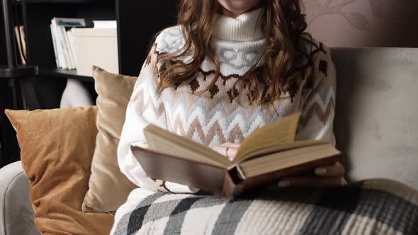 Woman Covered with Blanket Sits on Sofa and Reads Book