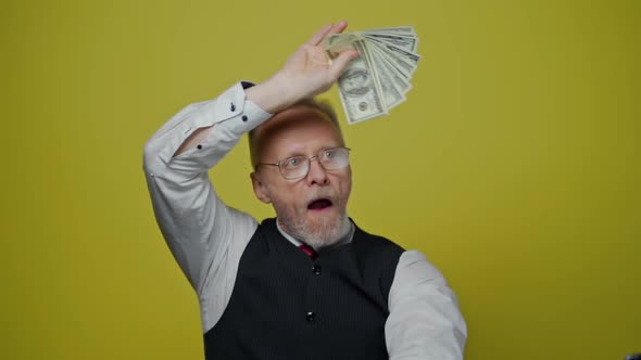 Funny senior man waving dollar banknotes. A lot of money in elderly man's hands.