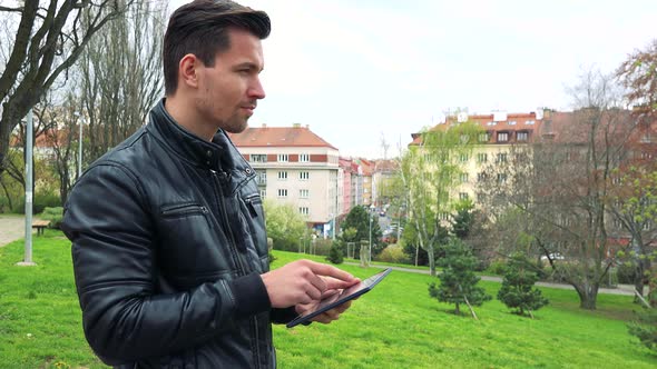 Young Handsome Man Stands, Works on Tablet Computer and Looks Around