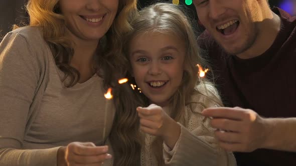 Cheerful Family Waving Bengal Lights, Sitting on Background of Christmas Tree