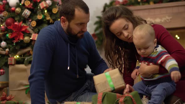 Mother, Father and Little Baby Sitting on the Floor in the Room with Christmas Decoration