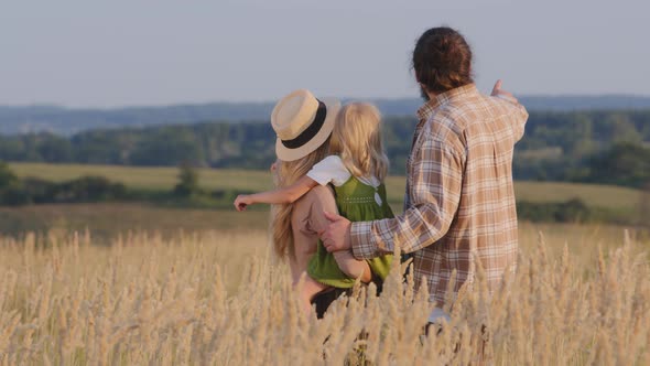 Back View Caucasian Happy Family Man Woman and Child Parents with Daughter Hugging Stand in Wheat