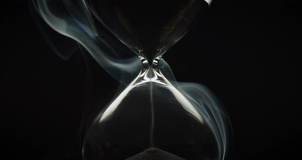 Smoke wraps an hourglass with black sand