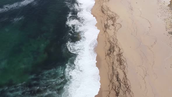 Arial shot flying along a beach and ocean waves.