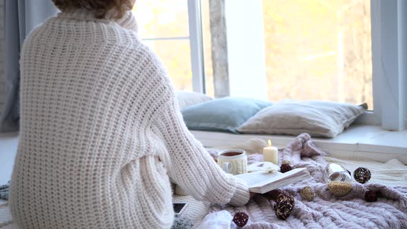 Lonely Woman In Knitted Sweater Sitting Alone At Window Reading Book