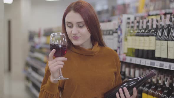 Portrait of Charming Redhead Caucasian Woman Smelling and Degustating Red Wine From Glass and