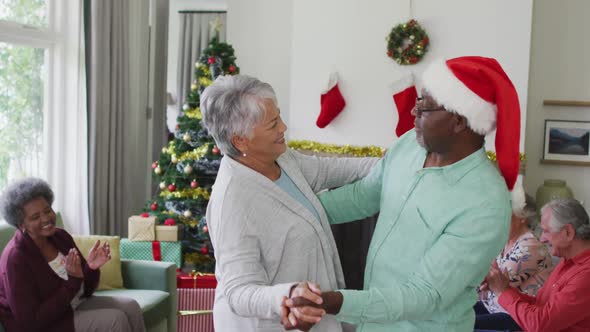 Happy diverse senior couple dancing together with friends in background at christmas time