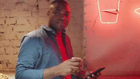 Black Man with Phone and Coffee Cup Posing in Loft Room