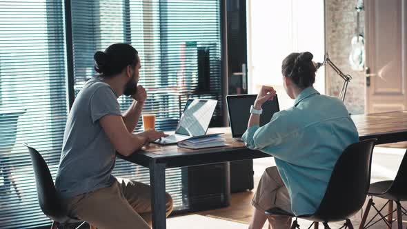 Two Coworkers are Discussing a Project While Sitting in Front of Their Laptops