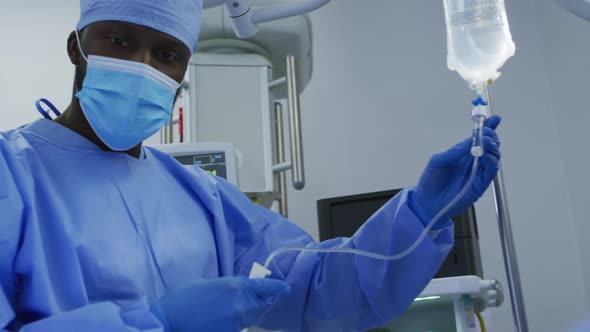 African american male surgeon wearing protective clothing prepating drip in operating theatre