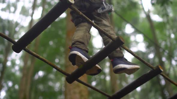 Superslowmotion Shot of a Little Boy in a Safety Harness Climbs on a Route in Treetops in a Forest