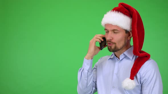 A Young Handsome Man in a Christmas Hat Talks on a Smartphone with a Smile - Green Screen Studio