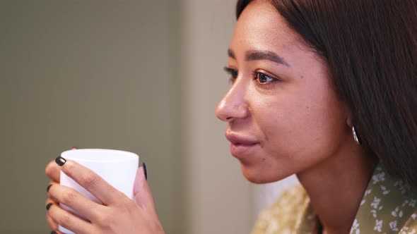 Meditative African woman wearing pajama drinking coffee