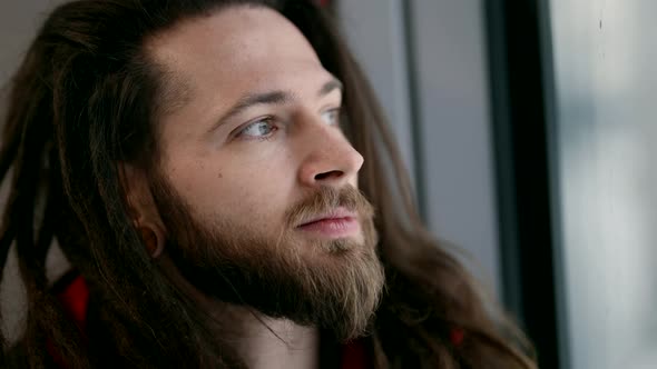 Portrait of Handsome Man with Beard and Long Hair Looking in Window When Riding Train