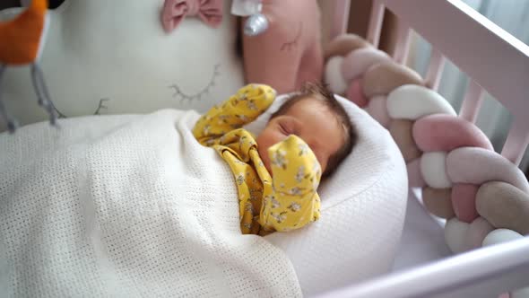 Newborn in a Yellow Jumpsuit Lies in a Retainer of the Child in a Crib