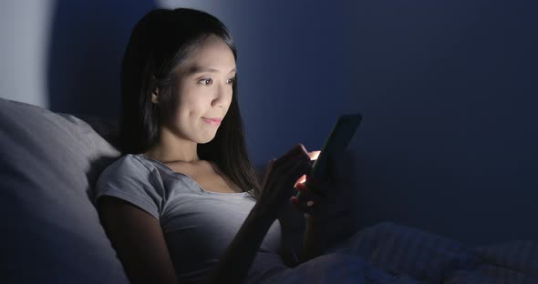 Woman use of mobile phone on bed at night 