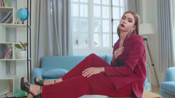 Young Fashion Transgender Woman Wearing Red Clothes Sitting On Table And Posing In Home