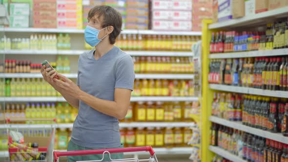 An Alarmed Man Wears a Medical Mask Against Coronavirus While Purchasing Food in a Supermarket or