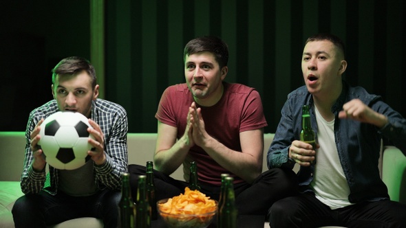 Three Handsome Happy Friendly Men Eating Chips Snacks and Cheering up for Football Game on TV