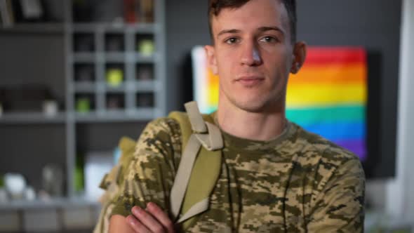 Live Camera Zoom Out As Confident Caucasian Gay Man Crossing Hands Posing Indoors with Rainbow Flag