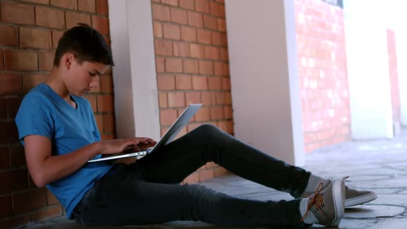 Schoolboy sitting in corridor and using laptop